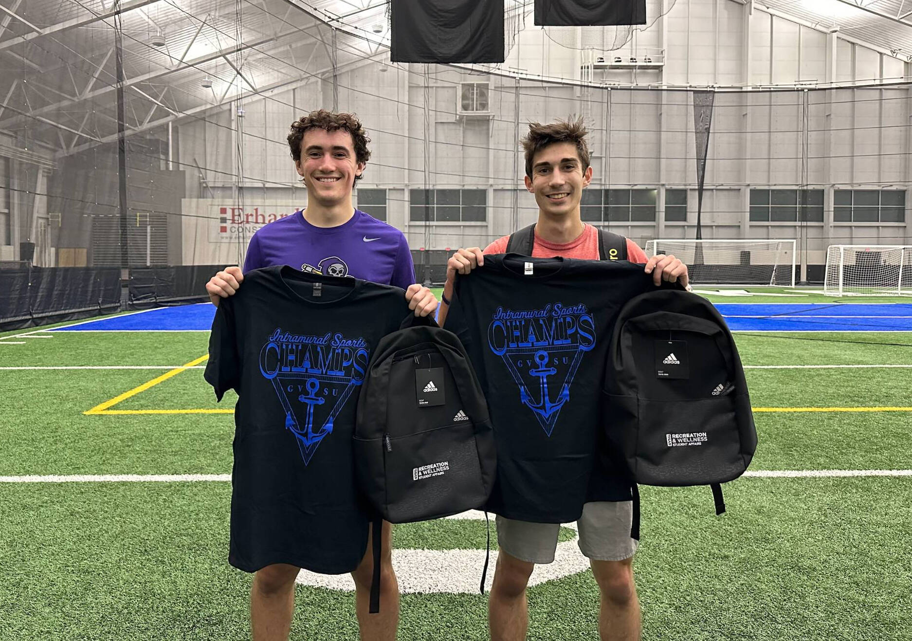 two men holding black tshirts and backpacks in front of them